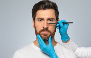 A plastic surgeon making marks on a man's nose explaining functional rhinoplasty procedure.